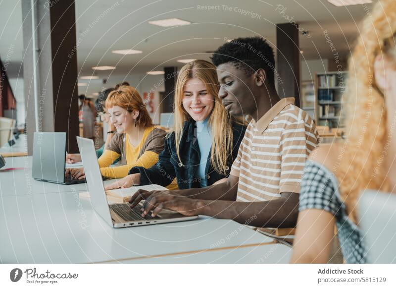 Fröhliche diverse Freunde, die in der Universität mit Laptops Aufgaben erledigen Schüler Prüfungsvorbereitung lernen Bibliothek benutzend Tippen Zusammensein