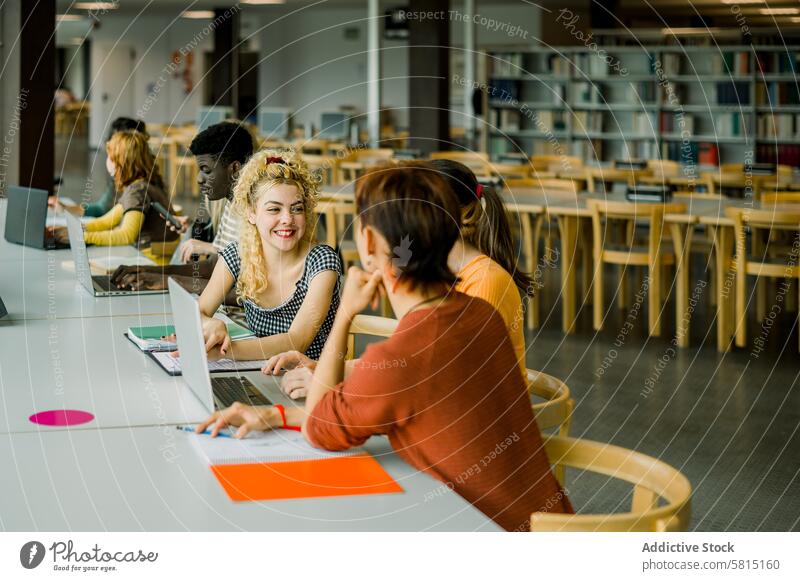 Eine Gruppe multiethnischer Studenten sitzt in der Bibliothek Menschengruppe Männer Frauen Schüler Gespräch diskutieren zusammenarbeiten lernen interagieren