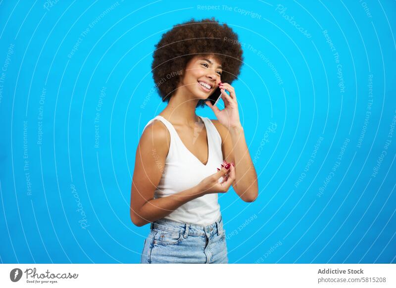 Junge Latina Frau mit Afro-Haar lächelnd im Gespräch auf einem Mobiltelefon blauen Hintergrund jung lateinamerikanisch Afro-Look Behaarung Lächeln sprechend