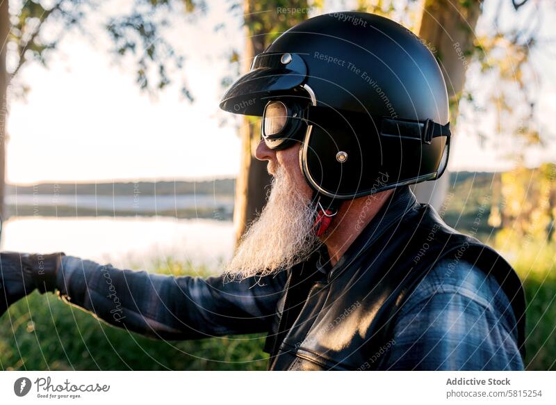 Senior Biker schaut weg, während er die Natur erkundet männlich Motorradfahrer Schutzhelm Schutzbrille Wegsehen Vollbart im Freien Entdecker Abenteuer Fahrrad