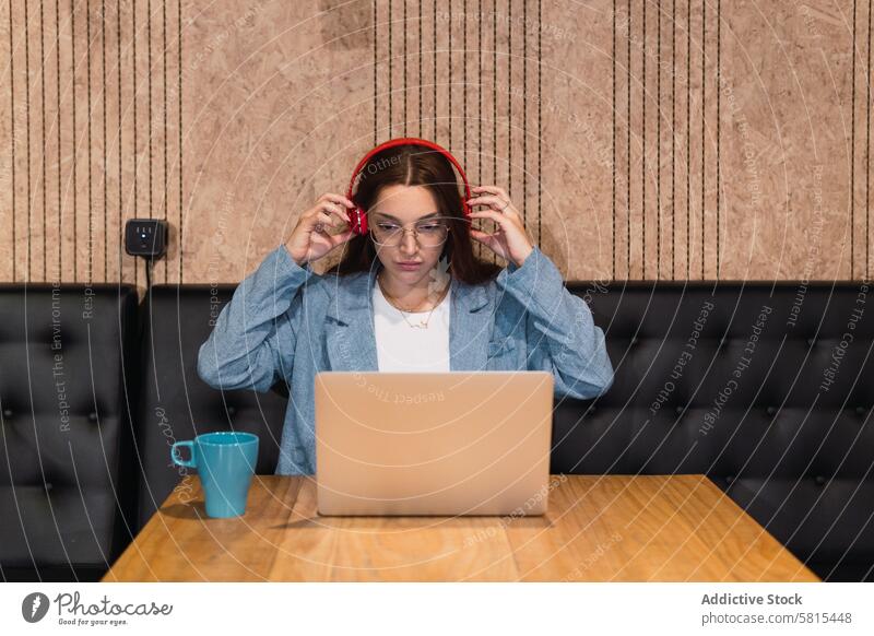 Freiberuflerin setzt Kopfhörer auf Geschäftsfrau angezogen vorbereiten freiberuflich Café ernst Laptop abgelegen Tisch Frau jung Heißgetränk zuhören Musik