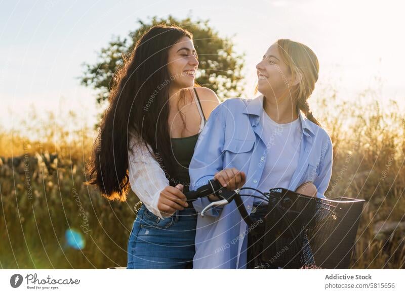 zwei junge Frauen auf einem Fahrrad in einem Feld bei Sonnenuntergang Lifestyle Sommer Natur Glück Himmel Mädchen Freizeit Menschen Paar Zusammensein