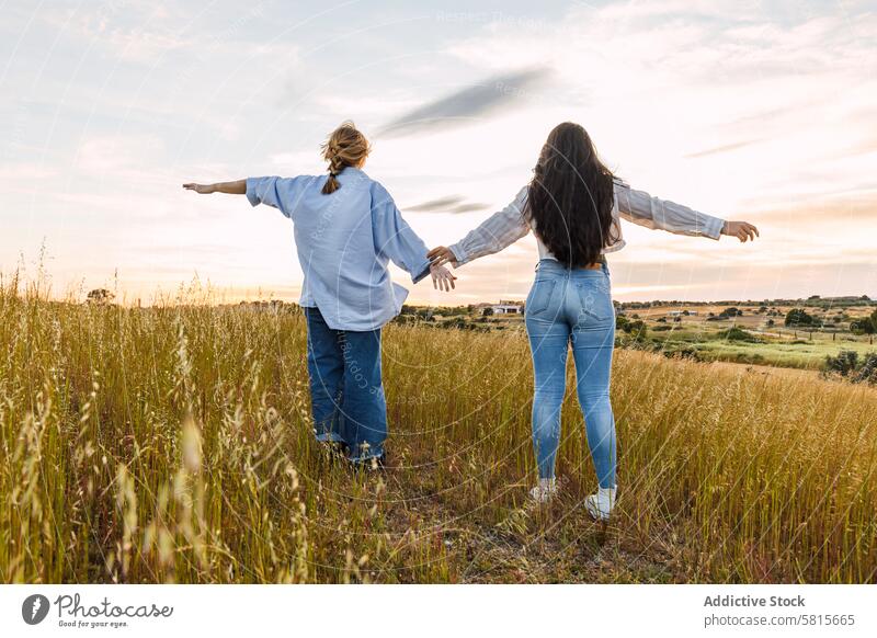 Zwei junge Frauen genießen die Natur mit offenen Armen, in einem Feld bei Sonnenuntergang Fröhlichkeit Liebe zwei Glück Kaukasier Zusammensein Freunde