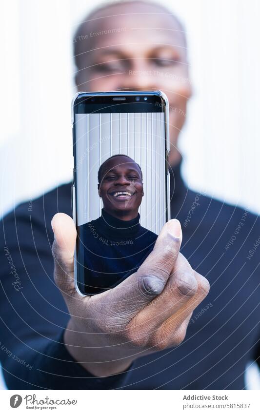 Fröhlicher afroamerikanischer Mann, der ein Selfie mit seinem Smartphone im Sonnenlicht macht Lächeln heiter Freude Bildschirm Straße genießen Selbstportrait