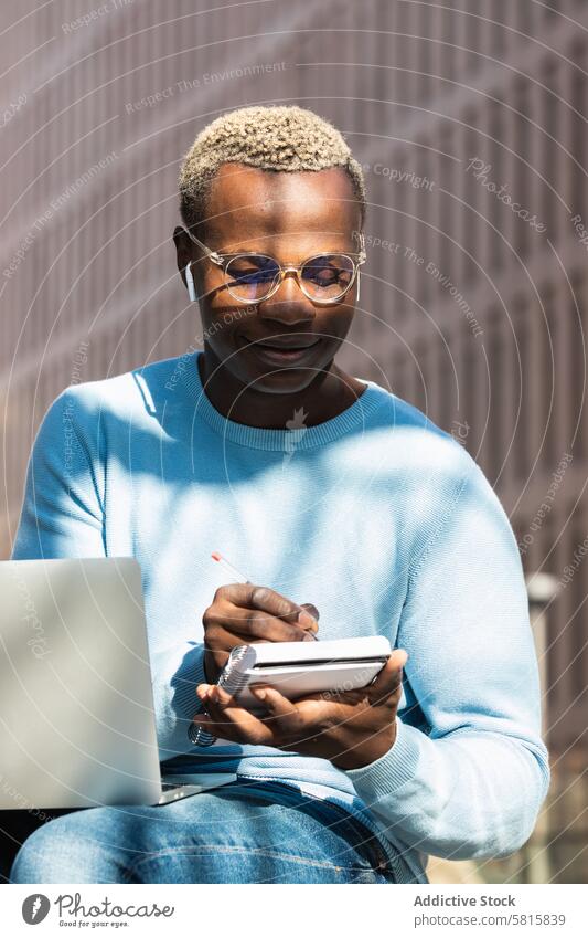 Positiver junger schwarzer männlicher Journalist, der sich während der Fernarbeit am Netbook Notizen macht Mann zur Kenntnis nehmen Arbeit Laptop Planer