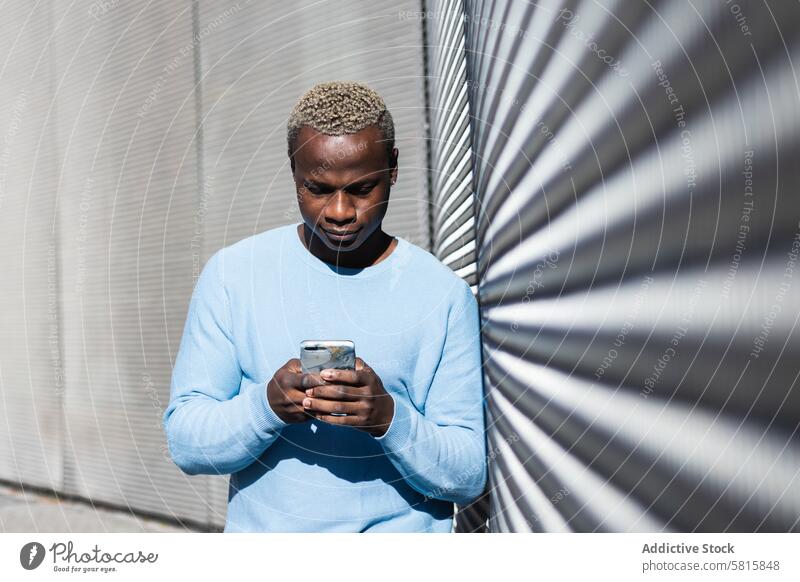 Junger Schwarzer, der auf der Straße sein Smartphone durchsucht Mann Freude Browsen zuschauend Texten Glück Optimist männlich jung ethnisch schwarz