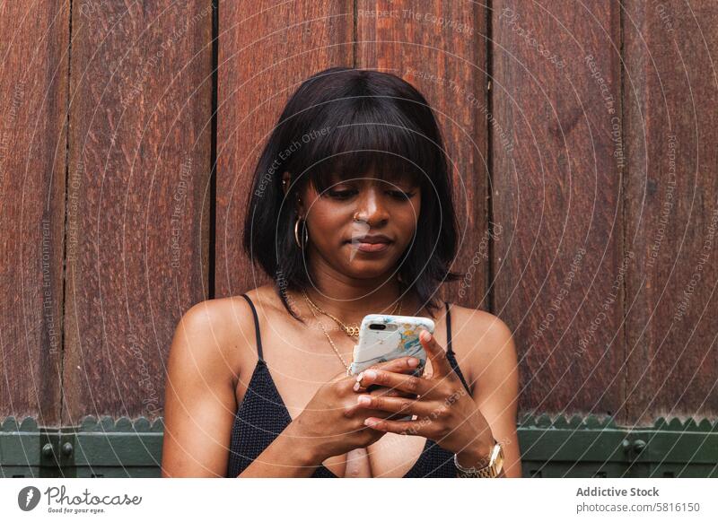 Schwarze Frau, die mit ihrem Smartphone chattet benutzend Dekolleté soziale Netzwerke positiv Spaß Moment Lächeln Gerät Apparatur Glück genießen Stil digital