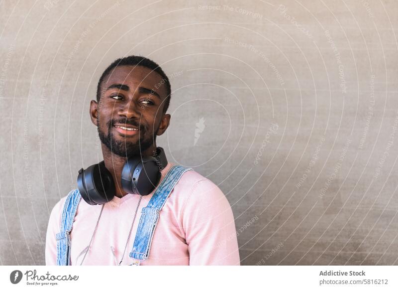 Lächelnder schwarzer Mann mit Kopfhörern auf der Straße cool Großstadt Vorschein trendy Outfit Drahtlos heiter männlich ethnisch Afroamerikaner Stil Glück