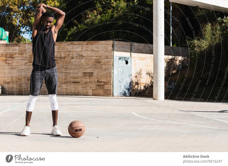 Schwarzer Sportler beim Stretching auf dem Basketballplatz Spieler Sportpark Dehnung Aufwärmen passen Ball Training Sommer strecken männlich schwarz