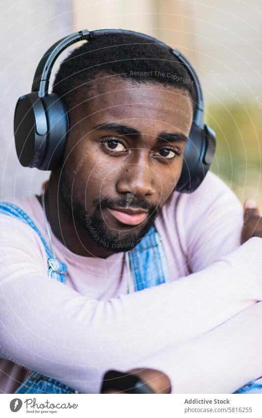 Stilvoller schwarzer Mann, der mit Kopfhörern Musik hört Hipster cool zuhören urban unabhängig Gesang männlich ethnisch Afroamerikaner Outfit Straße modern