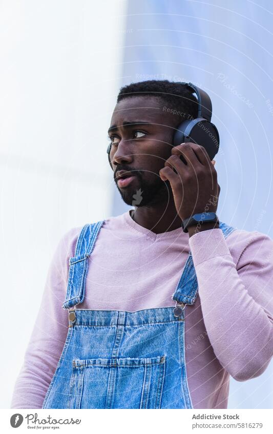 Stilvoller schwarzer Mann, der mit Kopfhörern Musik hört Hipster cool zuhören urban unabhängig Gesang männlich ethnisch Afroamerikaner Outfit Straße modern