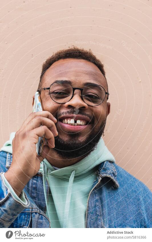 Fröhlicher schwarzer Mann, der in der Nähe der Wand telefoniert Smartphone reden heiter Lachen Hipster lässig Telefon Gespräch Kommunizieren Erwachsener