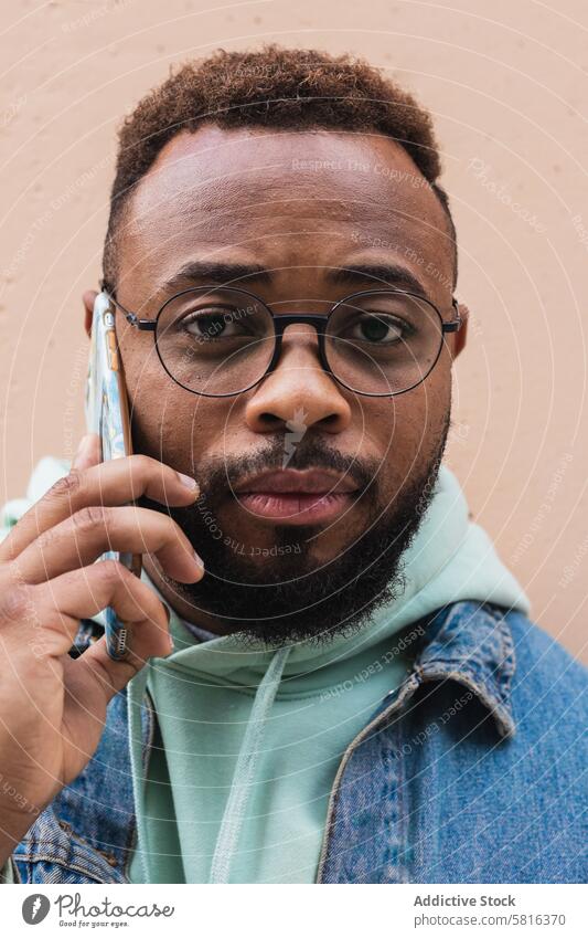 Schwarzer Mann spricht am Telefon in der Nähe der Wand Smartphone reden Hipster lässig Gespräch Kommunizieren Erwachsener Afroamerikaner schwarz ethnisch