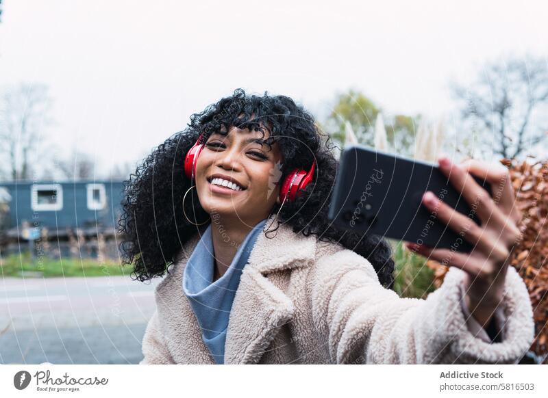 Schwarze Frau macht Selfie auf der Straße unter Smartphone Kopfhörer benutzend Musik zuhören Kälte afroamerikanische Frau schwarze Frau Großstadt Porträt
