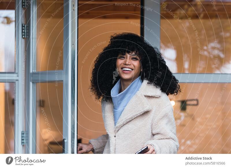 Glückliche schwarze Frau steht in der Tür eines Hauses heimwärts hinausgehend warme Kleidung Mantel Oberbekleidung Türöffnung urban afroamerikanische Frau