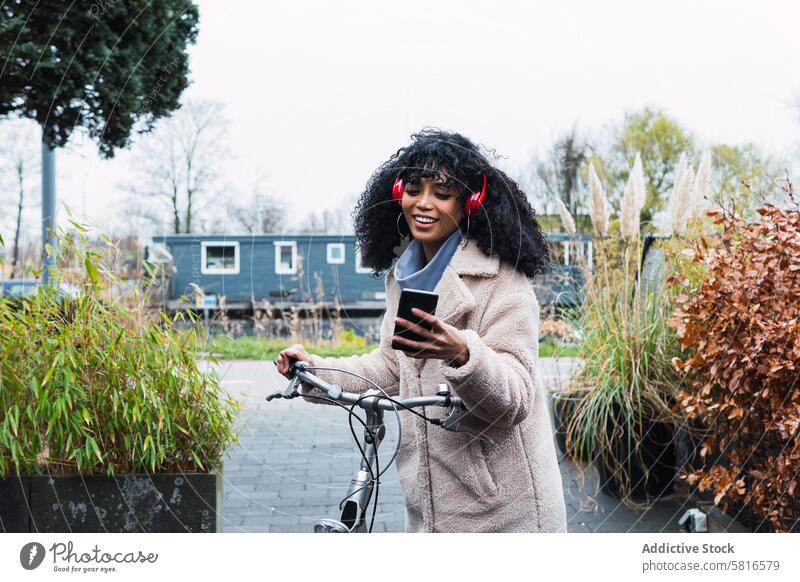 Schwarze Frau mit Smartphone auf dem Fahrrad Kopfhörer benutzend Musik zuhören Mitfahrgelegenheit Kälte afroamerikanische Frau schwarze Frau