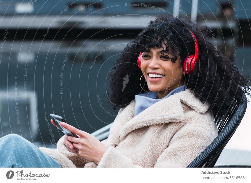 Fröhliche schwarze Frau, die am Seeufer Musik hört Kopfhörer Smartphone benutzend zuhören Kälte ruhen sich[Akk] entspannen Park afroamerikanische Frau Großstadt