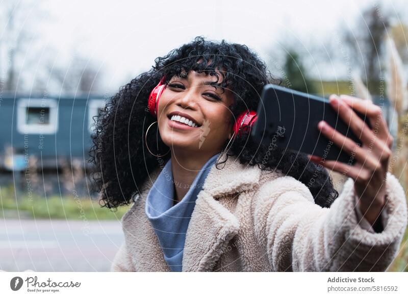 Schwarze Frau macht Selfie auf der Straße unter Smartphone Kopfhörer benutzend Musik zuhören Kälte afroamerikanische Frau schwarze Frau Großstadt Porträt