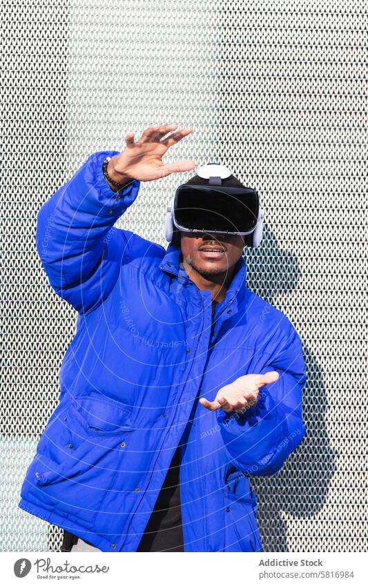 Schwarzer Mann erlebt die virtuelle Realität in der Stadt Virtuelle Realität Schutzbrille VR Brille Erfahrung interagieren berühren futuristisch Großstadt