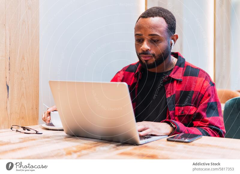 Schwarzer Mann arbeitet in einem Café an einem Laptop Kopfhörer benutzend online Internet Browsen freiberuflich Arbeit männlich schwarz Afroamerikaner Netbook