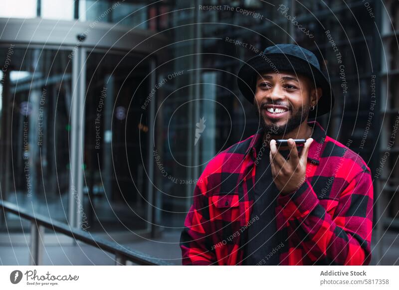 Fröhlicher schwarzer Mann spricht auf der Straße mit seinem Smartphone Sprachmeldung benutzend Großstadt Kommunizieren Audio online Internet urban männlich
