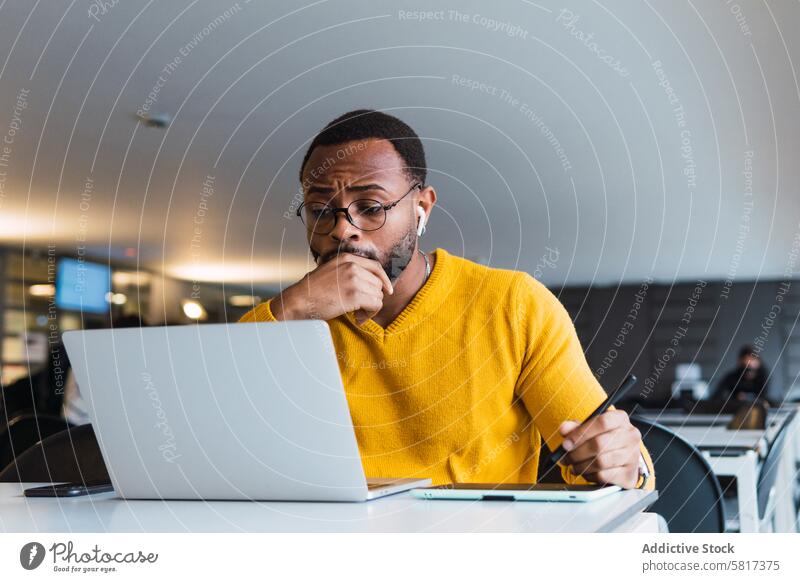 Schwarzer Mann arbeitet an Laptop mit Tablet Tablette Grafiktablett Designer Kopfhörer benutzend Arbeit online Internet Büro zur Kenntnis nehmen männlich