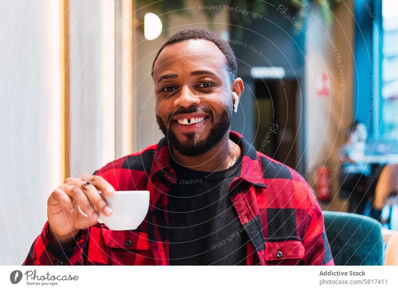 Lächelnder schwarzer Mann mit einer Tasse Kaffee im Cafe Café Kopfhörer benutzend Heißgetränk Kaffeepause Musik ruhen sich[Akk] entspannen männlich