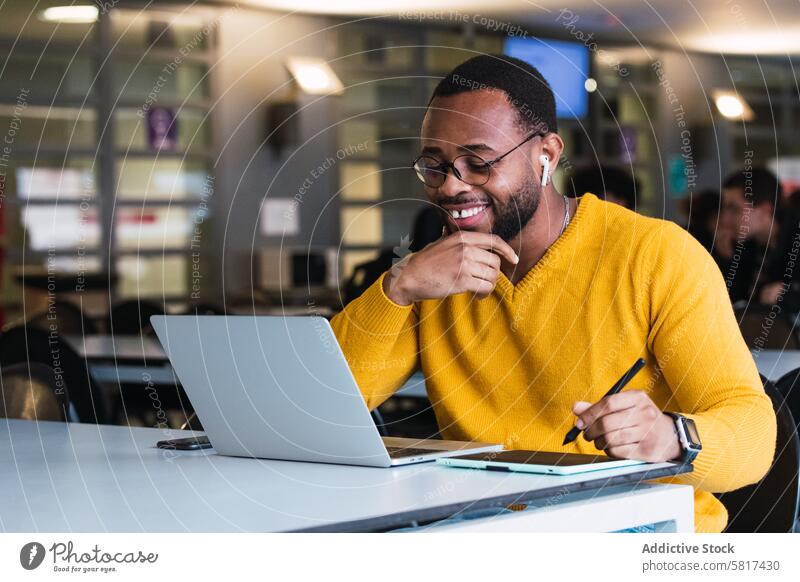 Lächelnder schwarzer Mann arbeitet am Laptop mit Tablet Tablette Grafiktablett Designer Kopfhörer benutzend Arbeit online Internet Büro zur Kenntnis nehmen