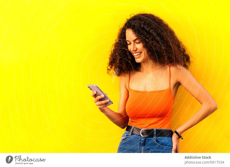 stylische Afro-Frau, die ihr Handy benutzt und sich an eine gelbe Wand lehnt Technik & Technologie jung Mobile Afro-Look Person Menschen Telefon Smartphone