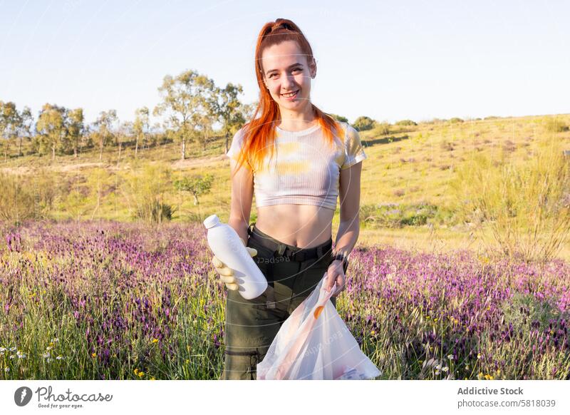 Junge Frau bei der Umweltsanierung auf einem Feld Erhaltung Säuberung Müll jung orangefarbenes Haar Flasche Müllsack im Freien Natur grün Freiwilliger Aktivität