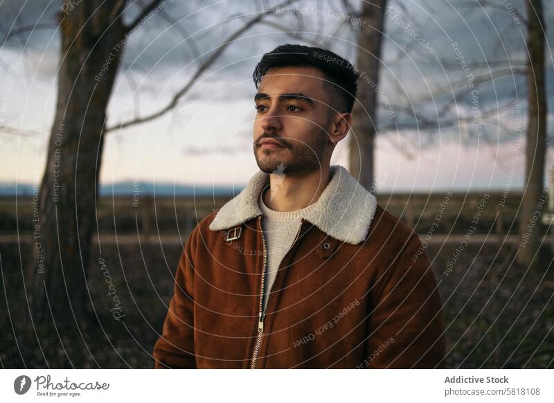 Porträt eines attraktiven Mannes in der Natur abschließen Jacke braun Vollbart Wegsehen Gesicht Ausdruck Bekleidung Baum Hintergrund Landschaft Lifestyle