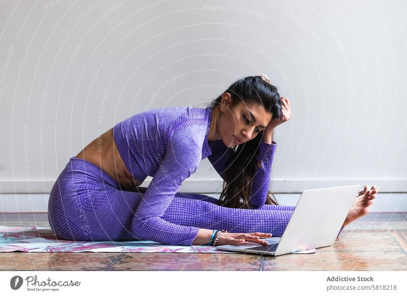 Flexible ethnische Frau mit Laptop beim Yoga-Training zu Hause benutzend Tutorial online positiv beweglich Achtsamkeit digital Wohlbefinden Internet jung