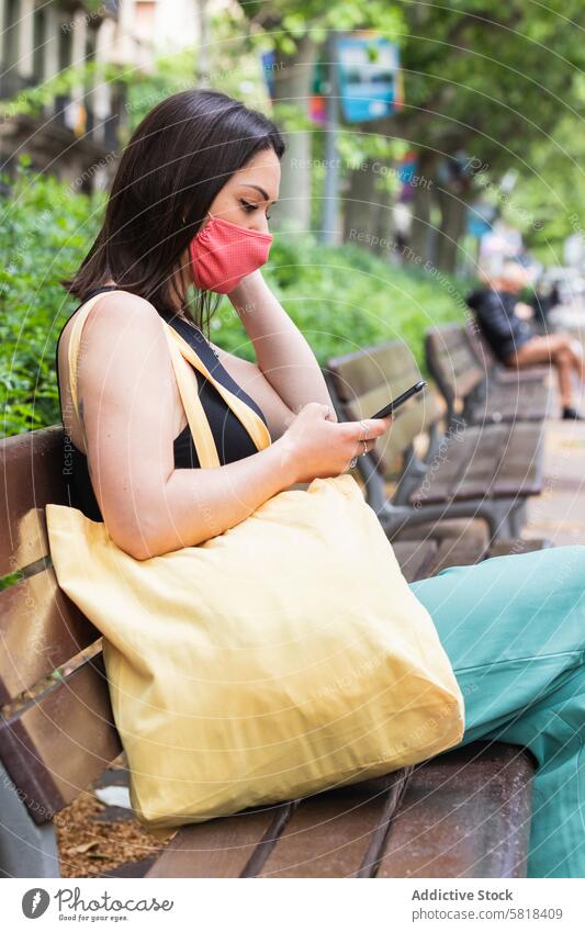 Frau mit Maske benutzt Smartphone in der Stadt während des Coronavirus benutzend Mundschutz neue Normale Großstadt Straße Browsen Bund 19 behüten Pandemie