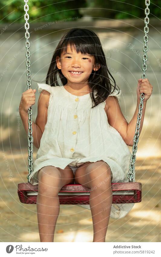 Fröhliches asiatisches Mädchen beim Schaukeln im Park während des Familienurlaubs pendeln Urlaub Ausflug Europa sonnig freudig Kind spielen im Freien Freizeit