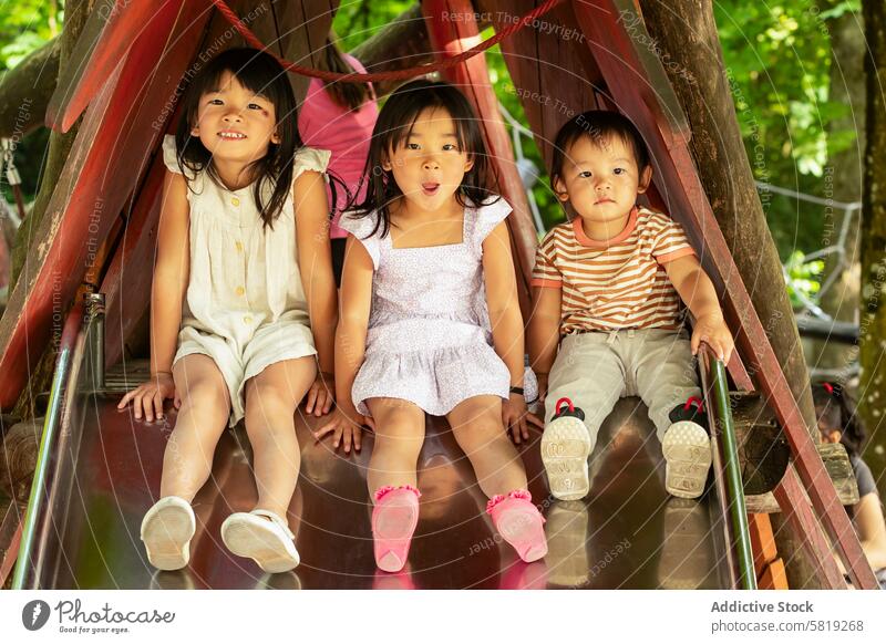 Asiatische Geschwister genießen eine Rutsche auf einem europäischen Spielplatz Kind Sliden Park Urlaub Europa Familie Spaß im Freien asiatisch Geschwisterkind