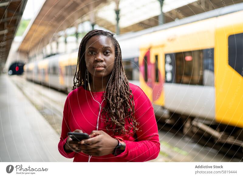 Schwarze Frau wartet am Bahnhof und benutzt ihr Smartphone Zug Station Warten Podest reisen Pendler Öffentlich Verkehr urban Großstadt Mobile Gerät hören Musik