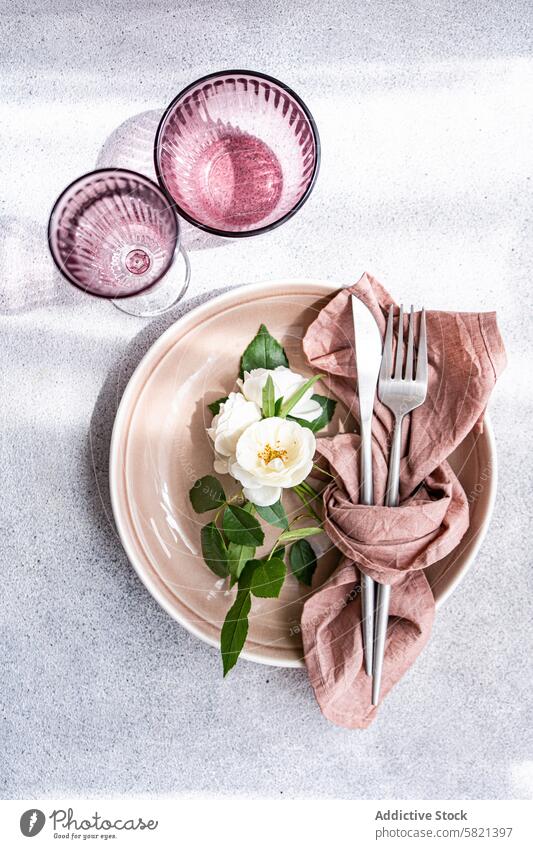 Elegantes Gedeck mit weißer Rose als Tafelaufsatz Tisch Roséwein Kernstück Teller Serviette Besteck Silberwaren Gabel Messer Eleganz speisend