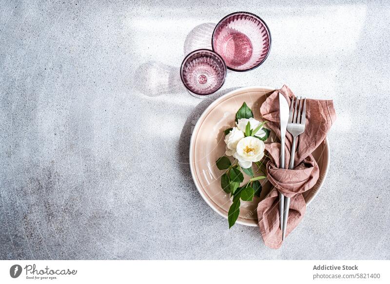 Elegant gedeckter Tisch mit weißen Rosen und rustikalen Tönen Einstellung Roséwein Utensil Teller beige texturiert Hintergrund elegant Dekor Essgeschirr Besteck