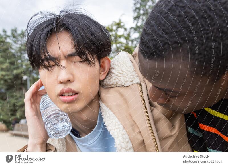 Junger Mann mit Hypoglykämie-Symptomen im Freien schwindelig unwohl Unterstützung Freund asiatisch Afrikanisch männlich Wasser Flasche Sorge Gesundheit