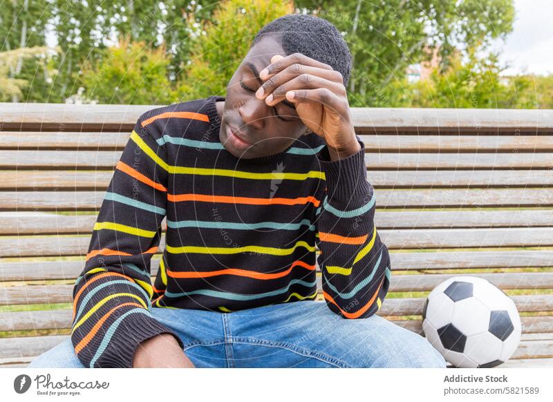 Junger Mann fühlt sich nach Fußballspiel schwindlig jung Schwindelgefühl Ball Bank Park Hypoglykämie Symptom überdrüssig müde Sport Aktivität physisch