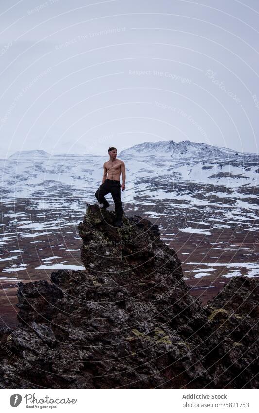 Mann steht ohne Hemd auf einem Felsvorsprung im verschneiten Island Felsen Berge u. Gebirge Schnee im Freien Abenteuer robust Landschaft Wildnis kalt Winter