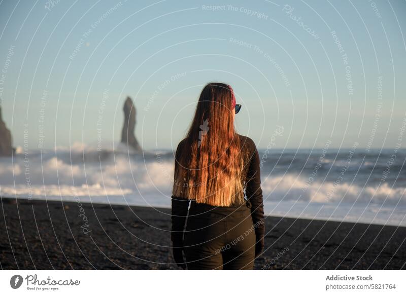 Frau mit Blick auf Meeresstapel am schwarzen Sandstrand von Island Strand schwarzer Sand Seeschornstein winken Küste Gelassenheit Morgen Natur reisen Einsamkeit