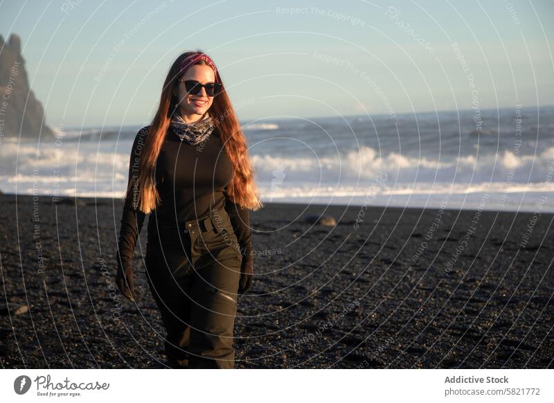 Junge Frau erkundet den schwarzen Sandstrand in Island Strand schwarzer Sand vulkanisch Sonnenbrille wandern lässig Stil im Freien Abenteuer reisen Tourismus