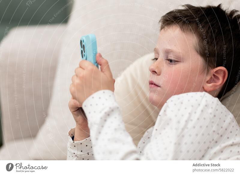 Junge zu Hause konzentriert auf Smartphone-Bildschirm Kind heimwärts Technik & Technologie räkeln Sofa sich[Akk] entspannen Freizeit im Innenbereich Gerät
