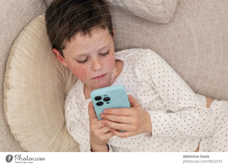 Junge vertieft in Smartphone zu Hause Kind heimwärts liegend Liege fokussiert im Innenbereich Technik & Technologie lässig Erholung Freizeit Bildschirmzeit