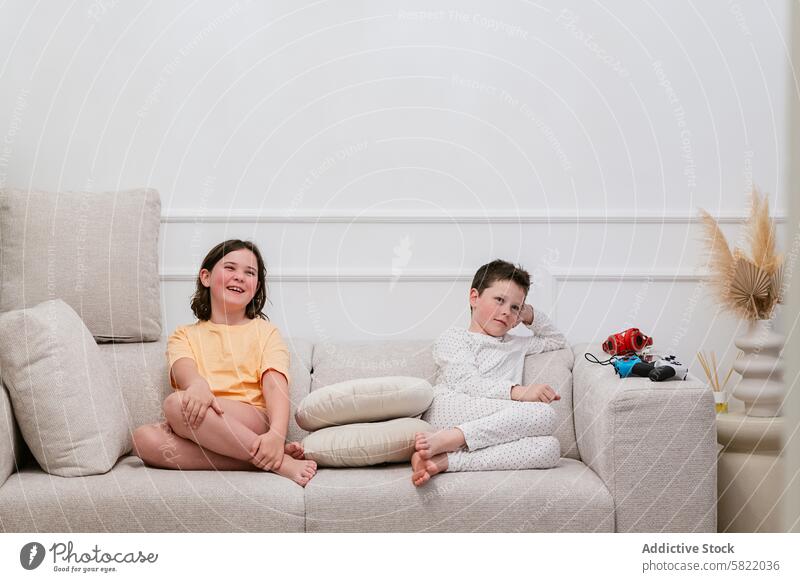 Geschwister, die zu Hause auf dem Sofa mit Spielzeug faulenzen Kind heimwärts Geschwisterkind Mädchen Junge Lachen in die Kamera schauen besinnlich Wegsehen