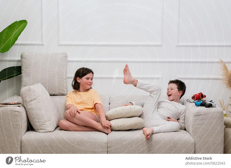 Geschwisterspaß auf der Couch, Mädchen beobachtet die Possen des Jungen Geschwisterkind Spaß Liege heimwärts Lachen zuschauend Vergnügen im Innenbereich