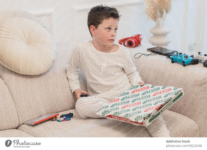 Lässiger Junge mit Pizza zu Hause, der wegschaut heimwärts Sofa Kasten lässig räkeln wegschauen Jugend Kind heimisch im Innenbereich Komfort gemütlich