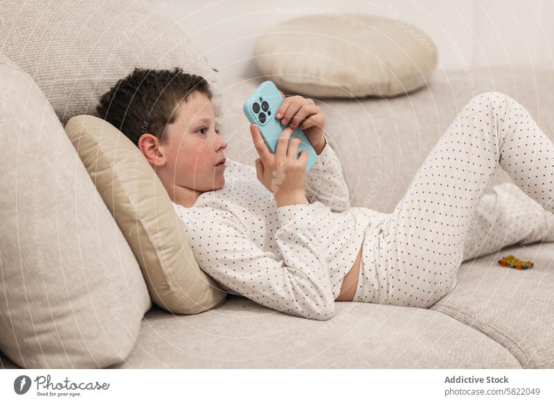 Junge entspannt mit Smartphone auf Couch Kind männlich heimwärts Liege Lügen entspannend absorbiert im Innenbereich Freizeit Bildschirm Technik & Technologie