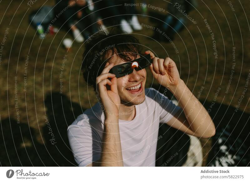 Junger Mann benutzt aufgeregt eine Sonnenfinsternisbrille im Freien jung solar Finsternis Brille Park Freund Menschengruppe heiter Natur Sammeln Sonnenlicht